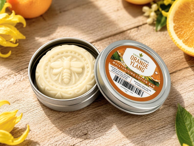 K&ouml;nnte beinhalten: Ein runder, cremefarbener Feuchtigkeits-Lotion-Riegel mit eingepr&auml;gtem Bienenmotiv in einer runden silbernen Metalldose. Der Deckel tr&auml;gt ein Etikett mit dem Text "seedgeeks ORANGE YLANG MOISTURIZING LOTION BAR" sowie einen Strichcode.