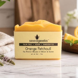 May include: A rectangular bar of orange soap wrapped in a light yellow paper label. The label features the text seedgeeks, PALM-FREE, VEGAN, HANDCRAFTED, Orange Patchouli, THE PERFECT BALANCE OF BRIGHT & EARTHY, and NET WT 4OZ - 5OZ.