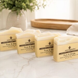 May include: Four rectangular bars of off-white soap wrapped in tan paper bands. Each band features the text seedgeeks, palm-free, vegan, coconut milk, Pure & Simple, and net wt 4oz. The soap bars are arranged in a diagonal line on a white surface.