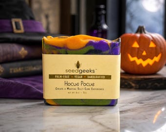 May include: A rectangular bar of soap with a marbled orange, purple, and green pattern. The label reads seedgeeks, palm-free, vegan, handcrafted, Hocus Pocus, create a magical self-care experience, and net wt 4oz - 5oz in black text.