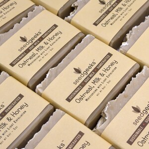 May include: Multiple rectangular bars of soap wrapped in tan paper labels. The labels feature the text seedgeeks, Sustainable, Goat Milk, Handcrafted, Oatmeal, Milk & Honey, Moisturizing with Light Exfoliation, and Net Wt 4oz - 5oz.