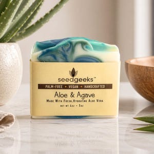 May include: A rectangular bar of soap with a marbled blue, green, and white top. The label reads seedgeeks, Palm-Free, Vegan, Handcrafted, Aloe & Agave, Made With Fresh, Hydrating Aloe Vera, and Net Wt 4oz - 5oz in black text on a tan background.
