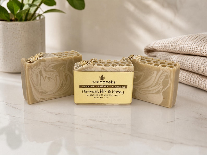 May include: Three rectangular bars of oatmeal, milk, and honey soap with a marbled beige and white pattern. The center bar features a gold label with the text seedgeeks, sustainable, goat milk, handcrafted, oatmeal, milk & honey, net wt 4oz - 5oz.