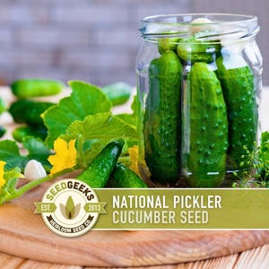 May include: A clear glass jar filled with green pickles. Fresh cucumbers, yellow flowers, and green leaves are arranged around a wooden cutting board. The text on the image reads "National Pickler Cucumber Seed" and "Seed Geeks".