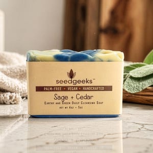 May include: A rectangular bar of soap with a light yellow and blue top, and a tan label. The label reads "seedgeeks" and "Sage + Cedar." The soap is palm-free, vegan, and handcrafted. Net weight is 4 oz.