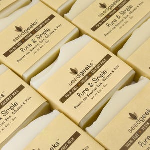 May include: Multiple rectangular bars of off-white soap wrapped in tan paper labels. The labels feature the text seedgeeks, Pure & Simple, Palm-Free, Vegan, Coconut Milk, and Net Wt 4oz - 5oz, printed in dark brown ink on a light background.