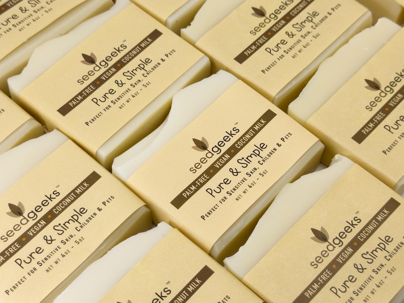 May include: Multiple rectangular bars of off-white soap wrapped in tan paper labels. The labels feature the text seedgeeks, Pure & Simple, Palm-Free, Vegan, Coconut Milk, and Net Wt 4oz - 5oz, printed in dark brown ink on a light background.