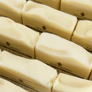 May include: Multiple rectangular bars of off-white soap arranged in a grid. Each bar is wrapped in a tan paper band featuring the text seedgeeks, palm-free, vegan, coconut milk, and Pure & Simple printed in a dark brown font.