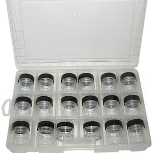 May include: A clear plastic storage case with 20 small clear glass jars with black lids. The case has a handle on the side and is open to reveal the jars.