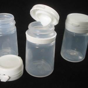 Peut inclure: Trois bouteilles en plastique transparent avec des couvercles blancs. Les bouteilles sont petites et rondes. Les couvercles ont un design à rabat.