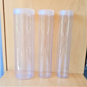 May include: Three clear plastic tubes of varying sizes. The tubes are cylindrical and have a smooth, transparent finish. They are arranged in a row from left to right, with the largest tube on the left and the smallest tube on the right.