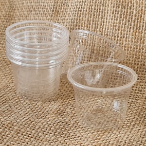 May include: A set of clear plastic cups, some stacked on top of each other, on a brown hessian background.