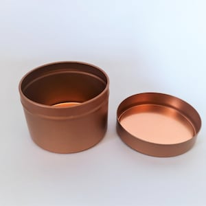 May include: A copper-coloured metal tin with a lid. The tin is round and has a smooth surface.