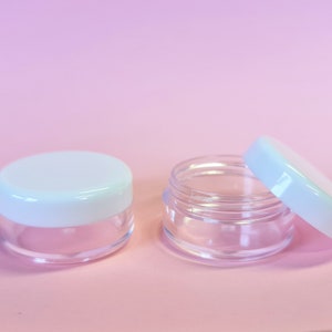 May include: Two clear plastic containers with white lids. The lids are slightly domed and have a smooth, glossy finish.
