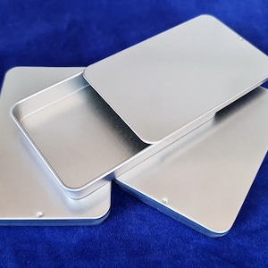 May include: Three silver metal rectangular boxes stacked on top of each other. The top box is open and the bottom two boxes are closed.