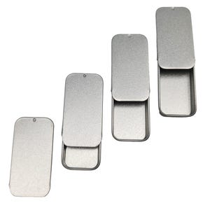 May include: Four silver metal tins with hinged lids. The tins are different sizes and are arranged in a row from largest to smallest.