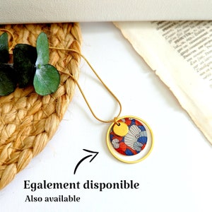 May include: A gold chain necklace with a round pendant featuring a red, blue, and white floral pattern. The pendant is surrounded by a gold circle.