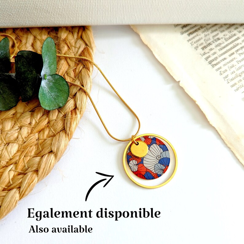 May include: A gold chain necklace with a round pendant featuring a red, blue, and white floral pattern. The pendant is surrounded by a gold circle.