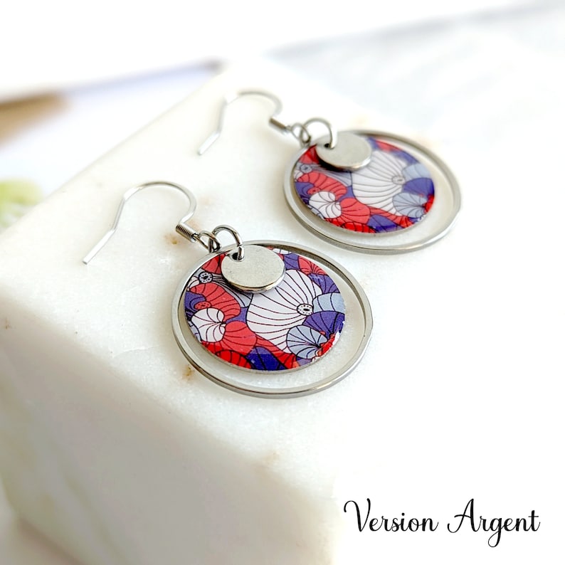 May include: Silver earrings with a round, patterned design featuring red, white, and purple colors. The earrings have a double circle design with a smaller circle in the center.