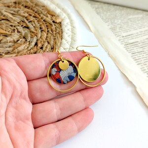 May include: Gold hoop earrings with a smaller circle pendant featuring a red, blue, and white floral pattern.