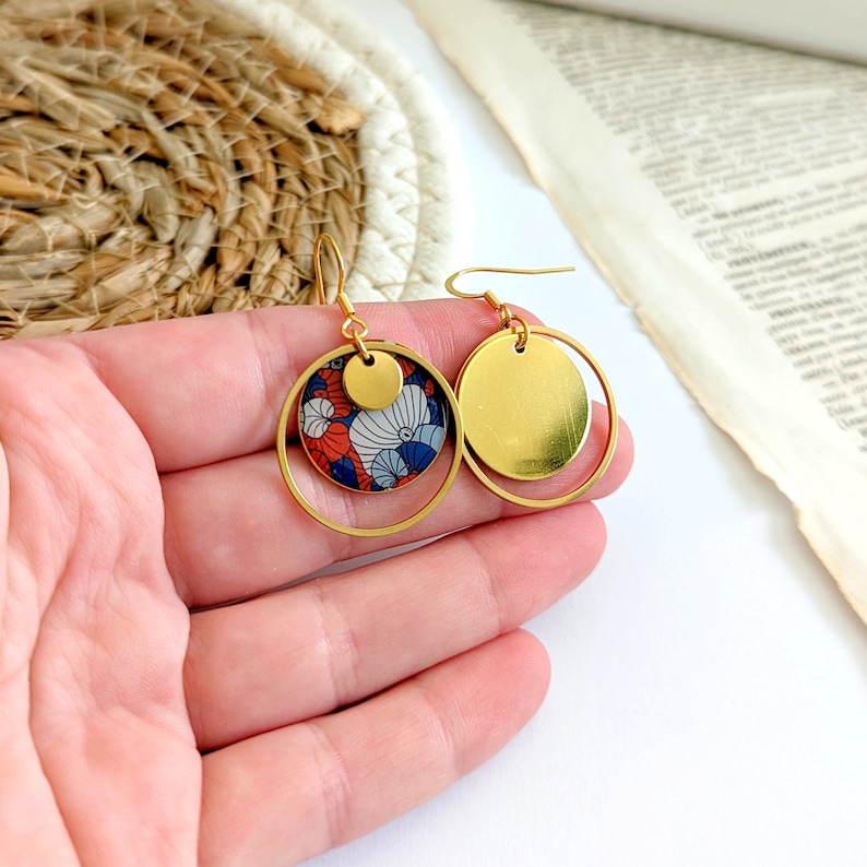 May include: Gold hoop earrings with a smaller circle pendant featuring a red, blue, and white floral pattern.