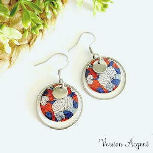 May include: Silver earrings with a double circle design. The inner circle features a red, white, and blue floral pattern. The outer circle is silver.