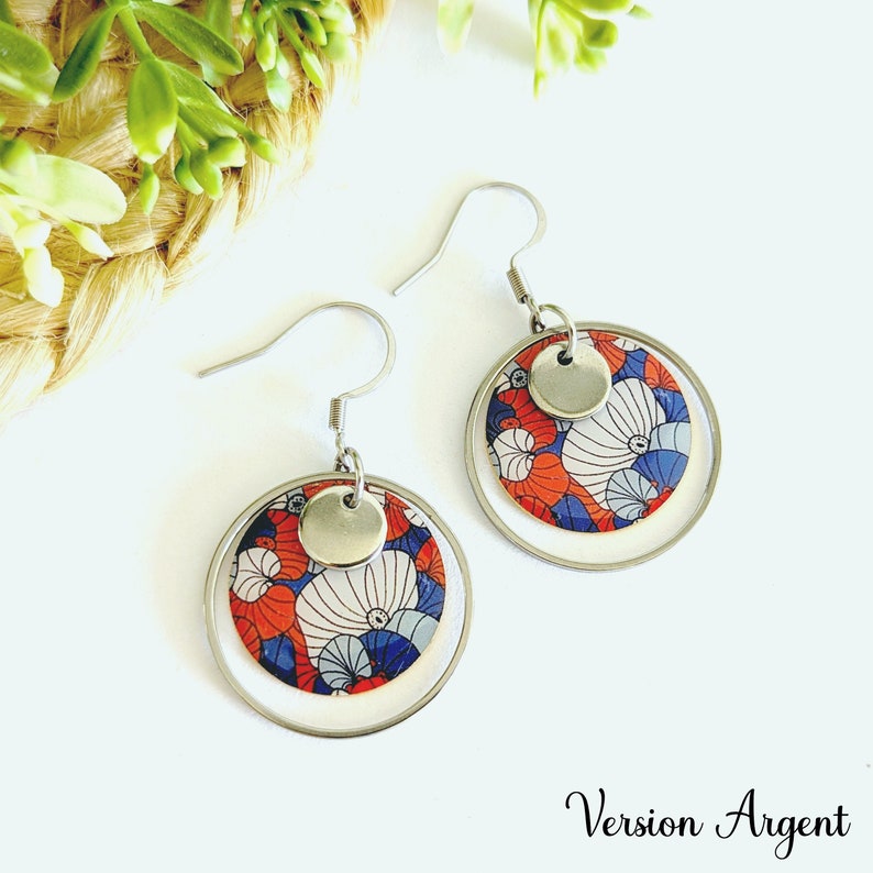 May include: Silver earrings with a double circle design. The inner circle features a red, white, and blue floral pattern. The outer circle is silver.