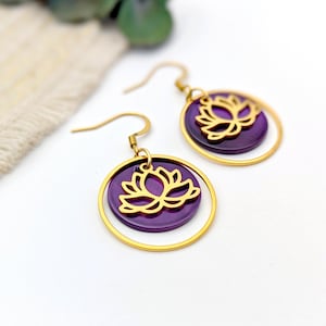 Peut inclure: Boucles d'oreilles dorées avec un motif de fleur de lotus violet. Les boucles d'oreilles sont en métal et ont une forme circulaire.
