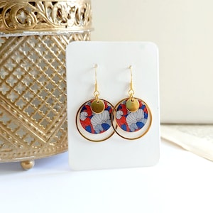 May include: Gold hoop earrings with a red, blue, and white patterned circle pendant. The pendant has a gold circle overlay.