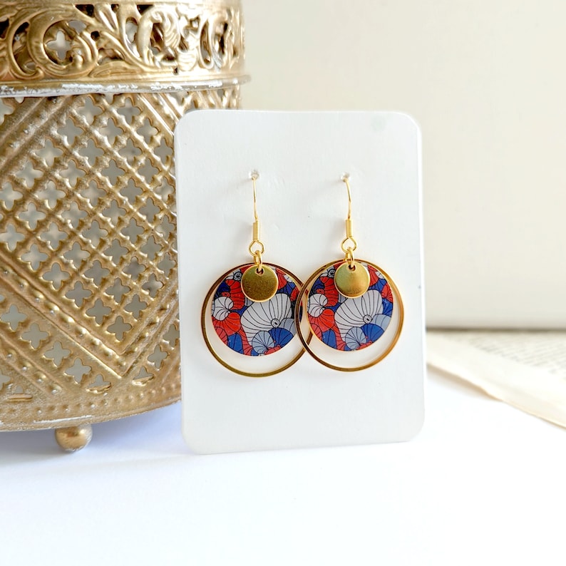May include: Gold hoop earrings with a red, blue, and white patterned circle pendant. The pendant has a gold circle overlay.