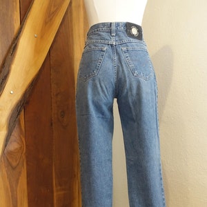 May include: A pair of blue denim jeans with a black leather patch on the back waistband that says "Versace Jeans Couture".