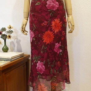 May include: A burgundy floral print skirt with a ruffled hem. The skirt features a pattern of large pink and orange flowers with green leaves. The skirt is displayed on a mannequin.