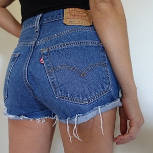 Könnte beinhalten: Eine blaue Jeans-Shorts mit ausgefransten Kanten und einem Levi's-Patch auf der Gesäßtasche. Die Shorts haben einen hohen Bund und eine lockere Passform.