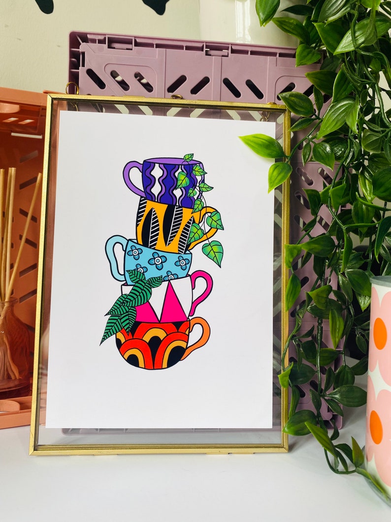 May include: A stack of four colorful mugs with geometric and floral patterns. The mugs are stacked on top of each other and a green plant is growing out of the top mug.