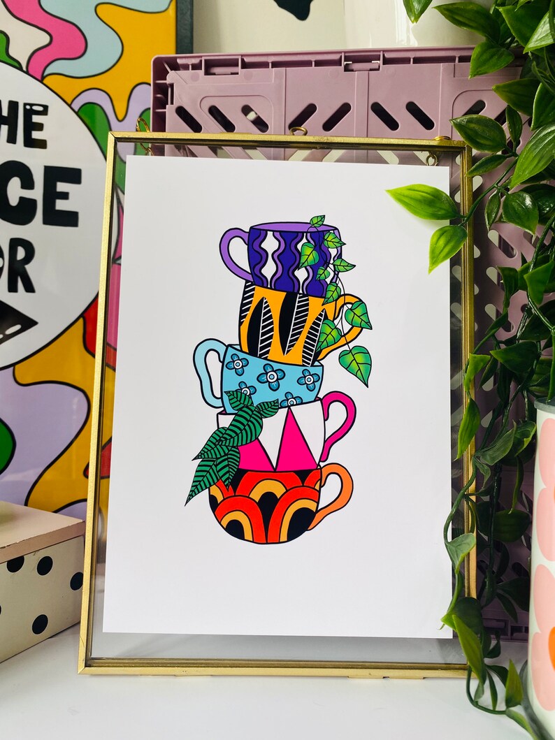 May include: A stack of four colorful mugs with different patterns, including a purple and white mug, a yellow and black mug, a blue and white mug, and an orange and black mug. The mugs are stacked on top of each other and have a green plant growing out of the top mug.