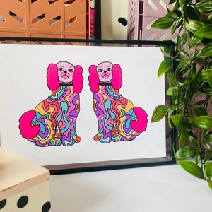 May include: A framed print of two colorful, psychedelic dogs with pink fur and black collars. The dogs are sitting and facing forward. The background is white.