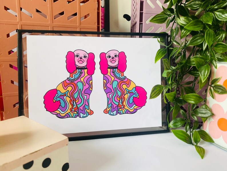 May include: A framed print of two colorful, psychedelic dogs with pink fur and black collars. The dogs are sitting and facing forward. The background is white.