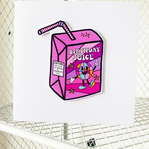 May include: A pink and purple birthday juice box with a cartoon character and the text "Birthday Juice". The box has a red and white striped straw.