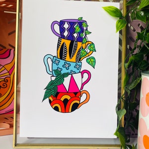 May include: A stack of four colorful mugs with geometric patterns, each with a different design. The mugs are stacked on top of each other, with a green plant growing out of the top mug. The mugs are set against a white background.