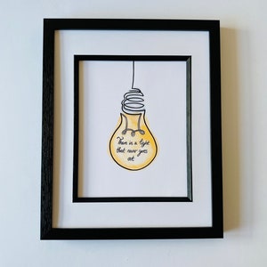 May include: A framed print with a yellow lightbulb drawn in black ink. The lightbulb has a quote inside that reads "There is a light that never goes out."