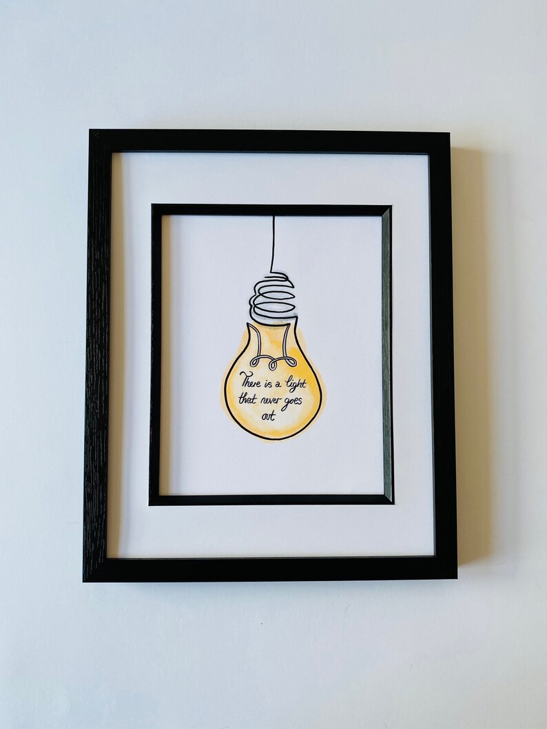 May include: A framed print with a yellow lightbulb drawn in black ink. The lightbulb has a quote inside that reads "There is a light that never goes out."