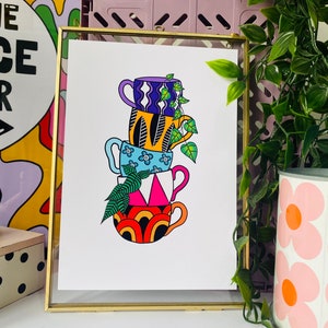 May include: A stack of four colorful mugs with different patterns, including a blue mug with white flowers, a yellow mug with black feathers, a purple mug with white wavy lines, and a red and orange mug with a rainbow pattern. A green vine with leaves is growing out of the top mug.