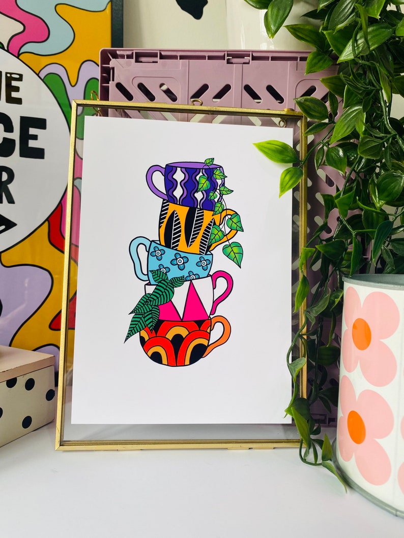 May include: A stack of four colorful mugs with different patterns, including a blue mug with white flowers, a yellow mug with black feathers, a purple mug with white wavy lines, and a red and orange mug with a rainbow pattern. A green vine with leaves is growing out of the top mug.