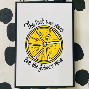 K&ouml;nnte beinhalten: Ein wei&szlig;er gerahmter Druck mit schwarzem Text, der "The past was yours but the future's mine." lautet. Eine gelbe Zitronenillustration ist mittig auf dem Druck platziert.