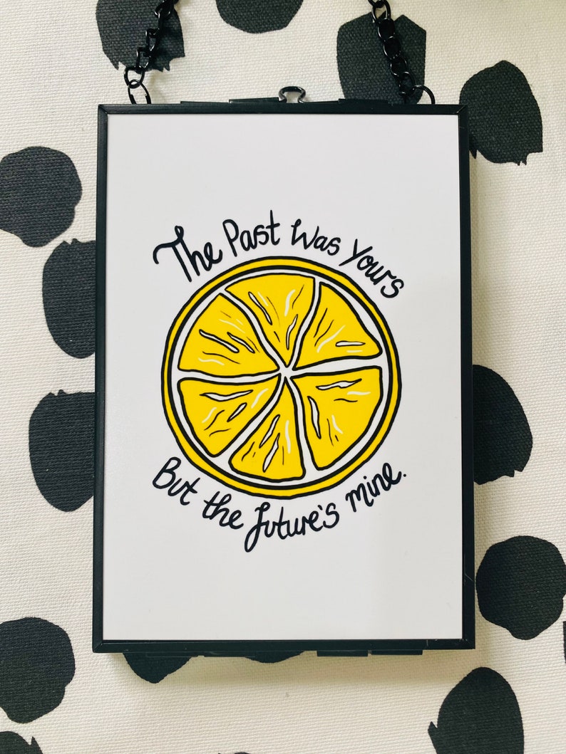 K&ouml;nnte beinhalten: Ein wei&szlig;er gerahmter Druck mit schwarzem Text, der "The past was yours but the future's mine." lautet. Eine gelbe Zitronenillustration ist mittig auf dem Druck platziert.