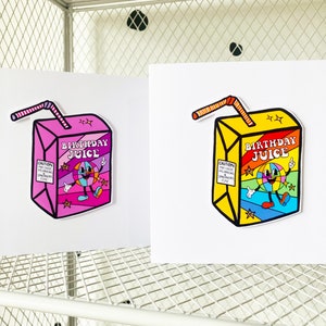 May include: Two illustrated cards with a cartoon juice box design. The juice box is yellow with a rainbow design and the text "Birthday Juice". The other juice box is pink with a rainbow design and the text "Birthday Juice".