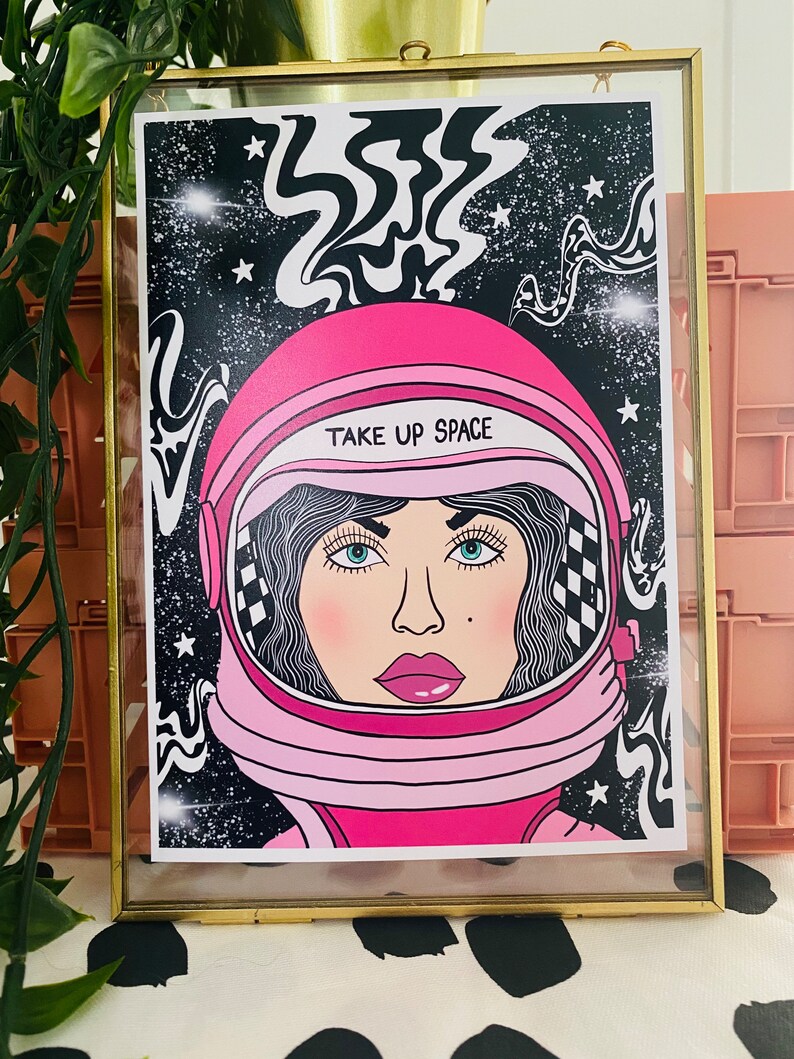 May include: A pink astronaut helmet with a black and white swirl design in the background. The helmet has a white visor and the text "TAKE UP SPACE" on the front.