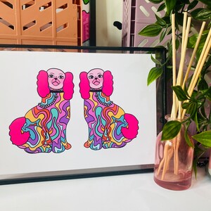 May include: A framed print of two colorful, psychedelic dogs with pink fur and swirling patterns. The dogs are facing forward and have black eyes and pink noses.