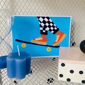 Pu&ograve; includere: Uno skateboard con stampa a scacchi blu e bianca con scarpe da ginnastica arancioni e gialle in cima. Lo skateboard &egrave; su uno sfondo blu con ruote gialle.