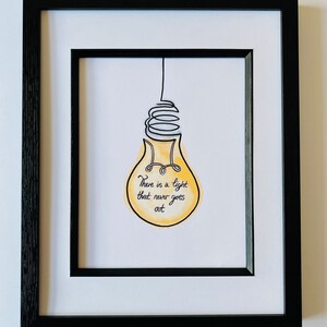 May include: A black framed print with a white mat. The print features a yellow light bulb with a black wire and the text "There is a light that never goes out."